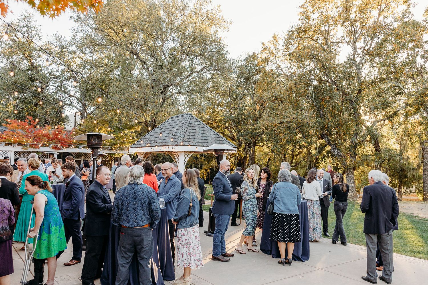 Large group of wedding guests gathered outdoors under autumn trees.