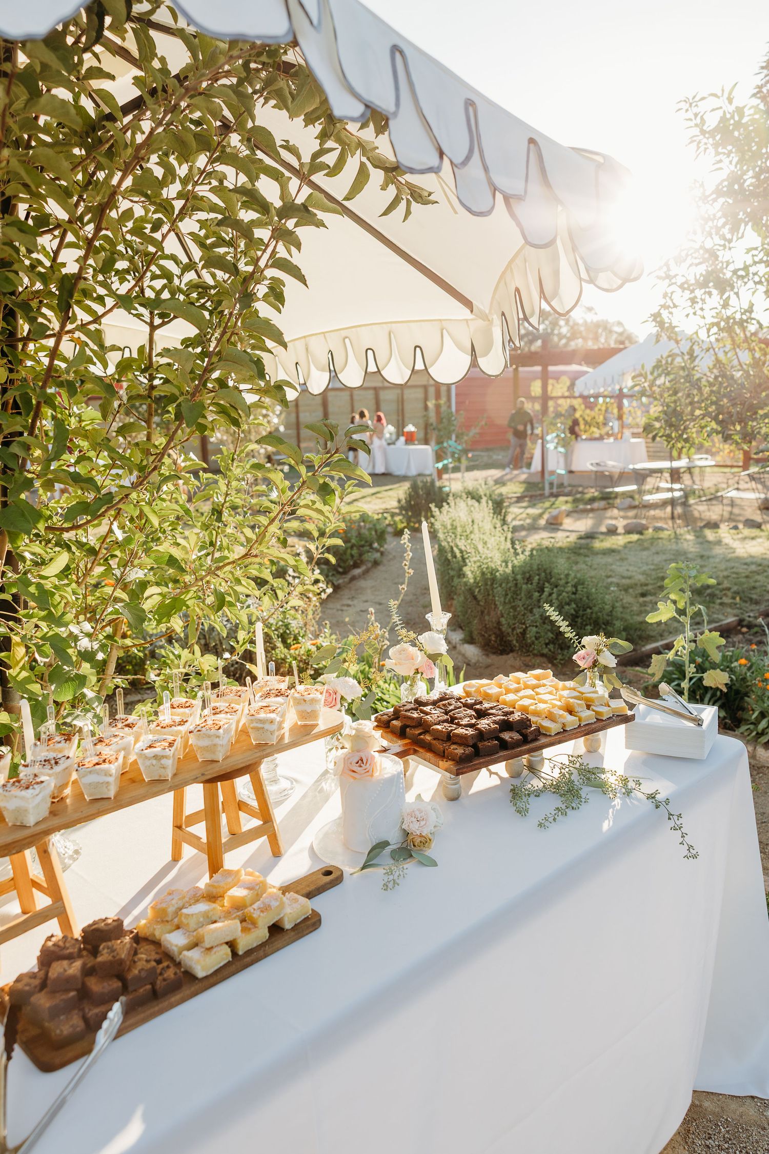 Elegant wedding reception buffet table with desserts under outdoor tent lighting.