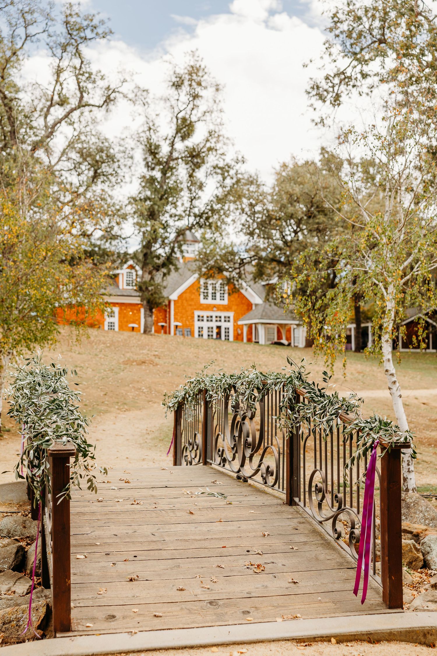 Rustic wooden boardwalk path leading to red cabins on a hillside surrounded by autumn trees.