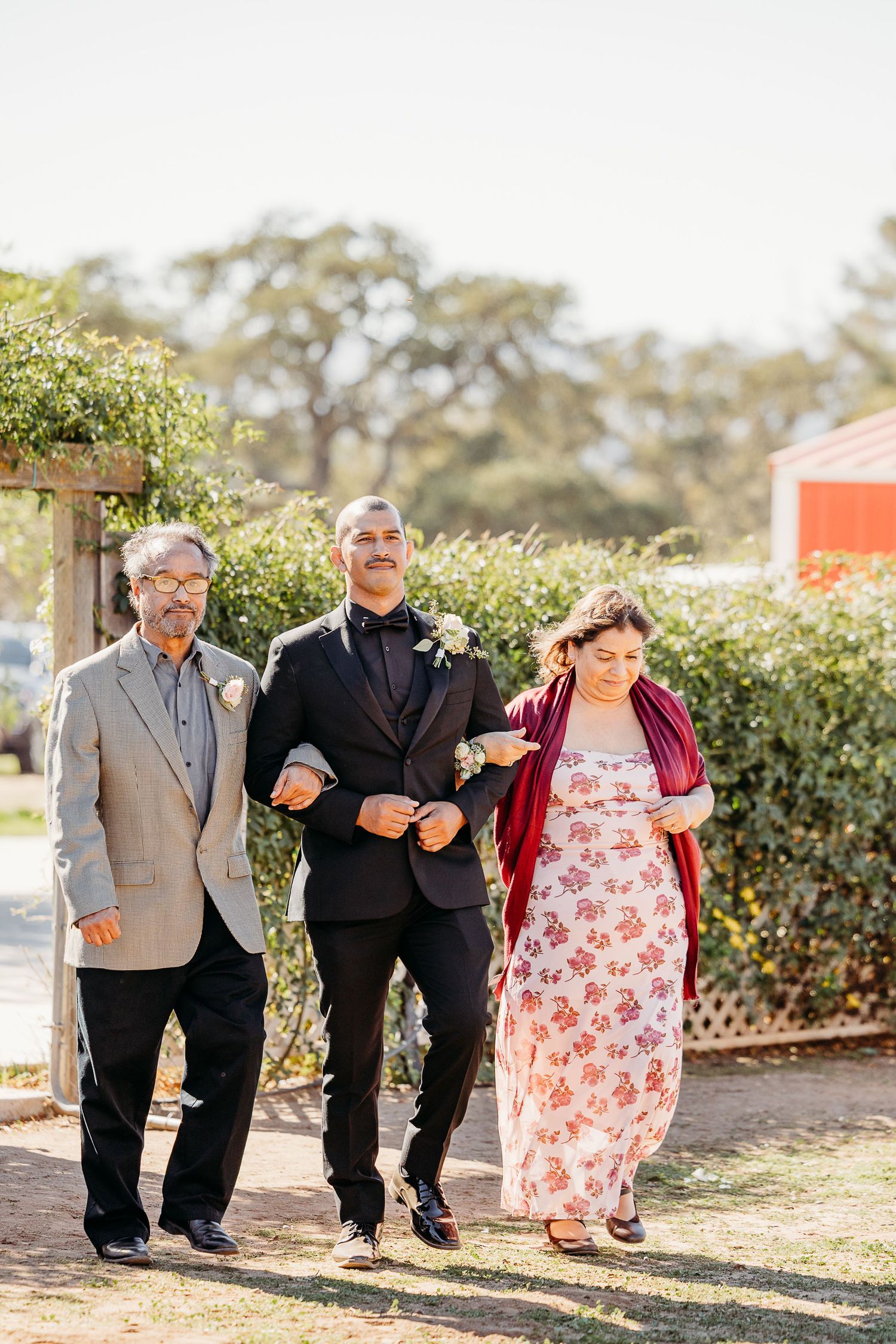 Three people walking down a garden path at an outdoor wedding ceremony.