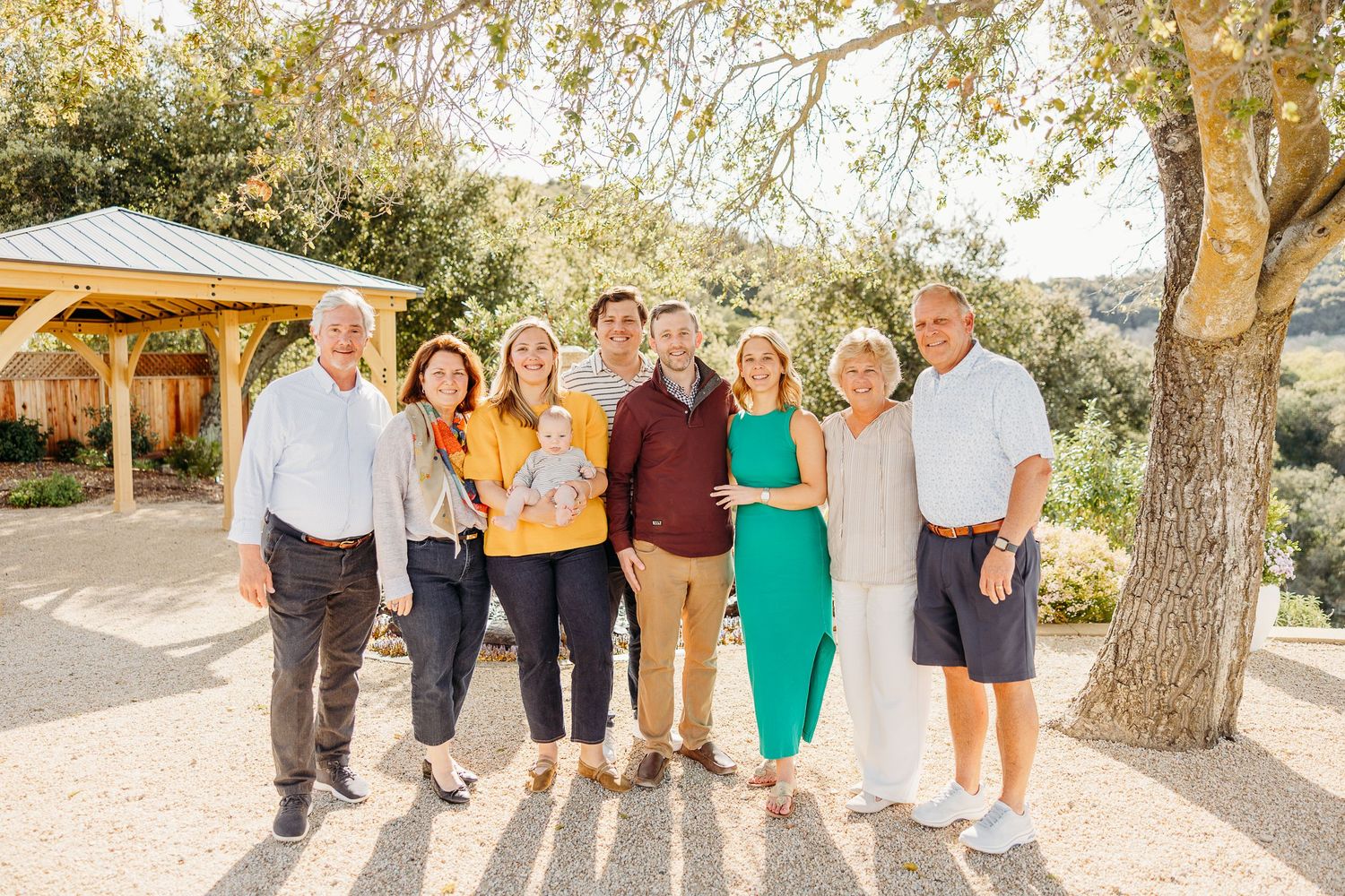 Family members pose together outdoors under a tree during a professional photo session.