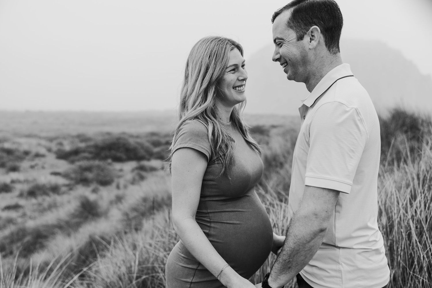A happy couple shares a joyful moment during their maternity session on a hillside.