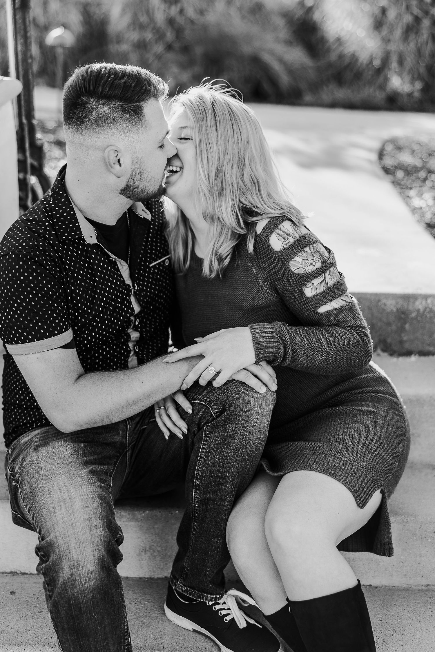 A black and white portrait of a couple sharing an affectionate moment on steps.