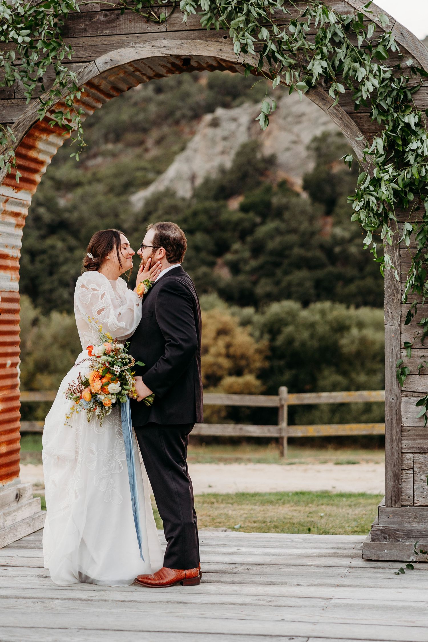 Romantic wedding couple sharing an intimate moment under a rustic stone arch adorned with greenery and flowers best San Luis Obispo wedding.