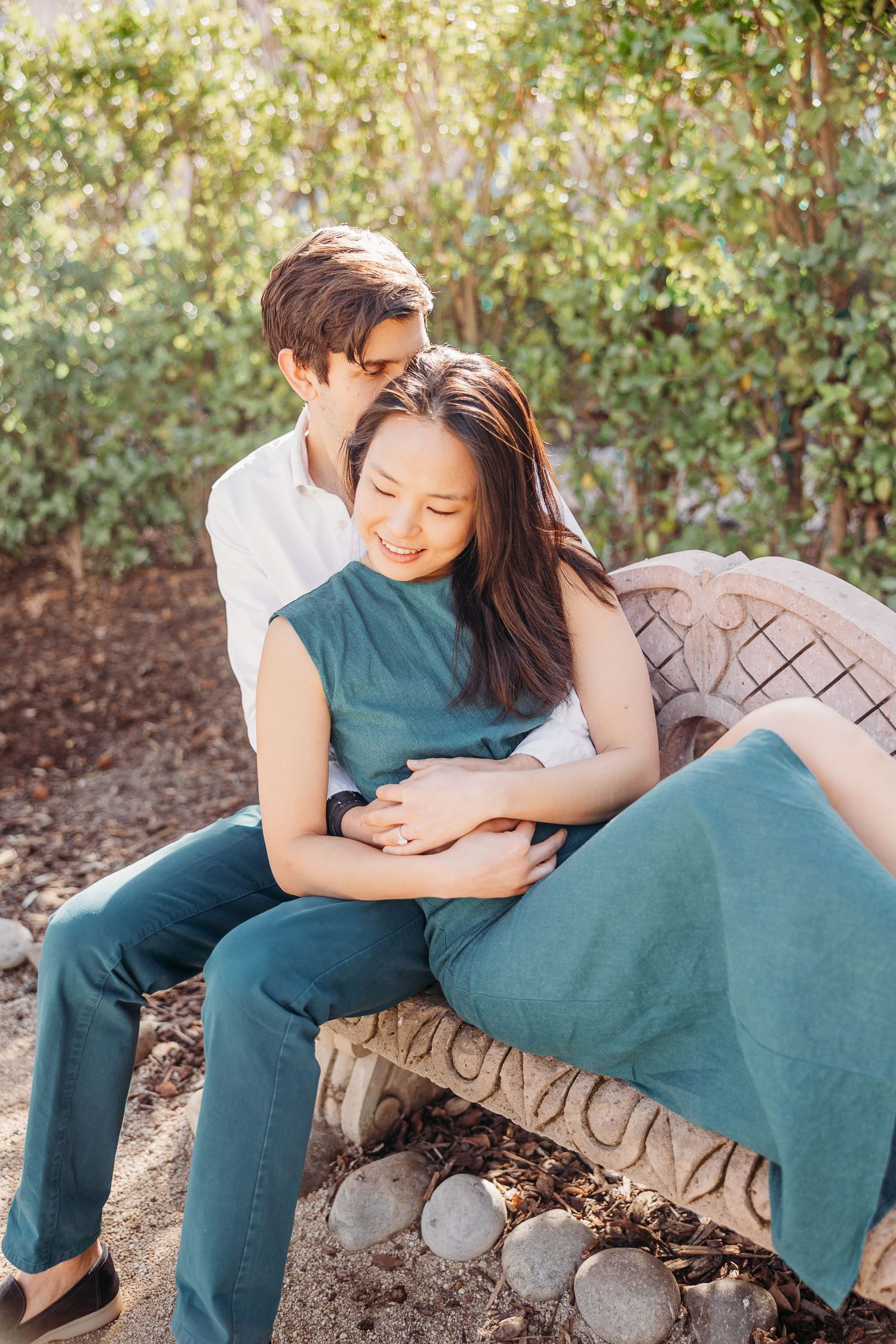 A couple relaxing together on an outdoor bench surrounded by greenery and natural light.
