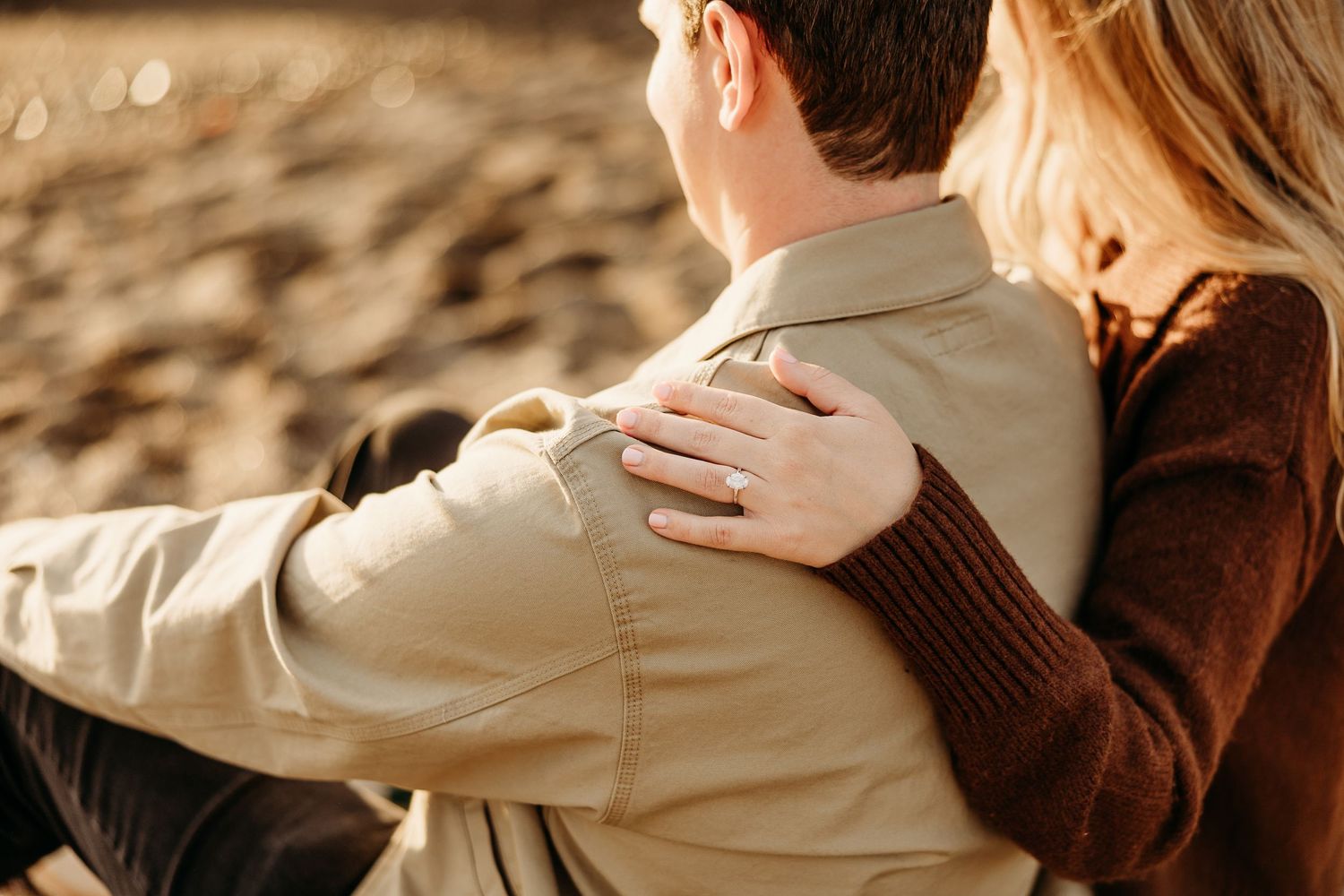 Close-up details of couple embracing on beach wearing brown and beige casual outfits.