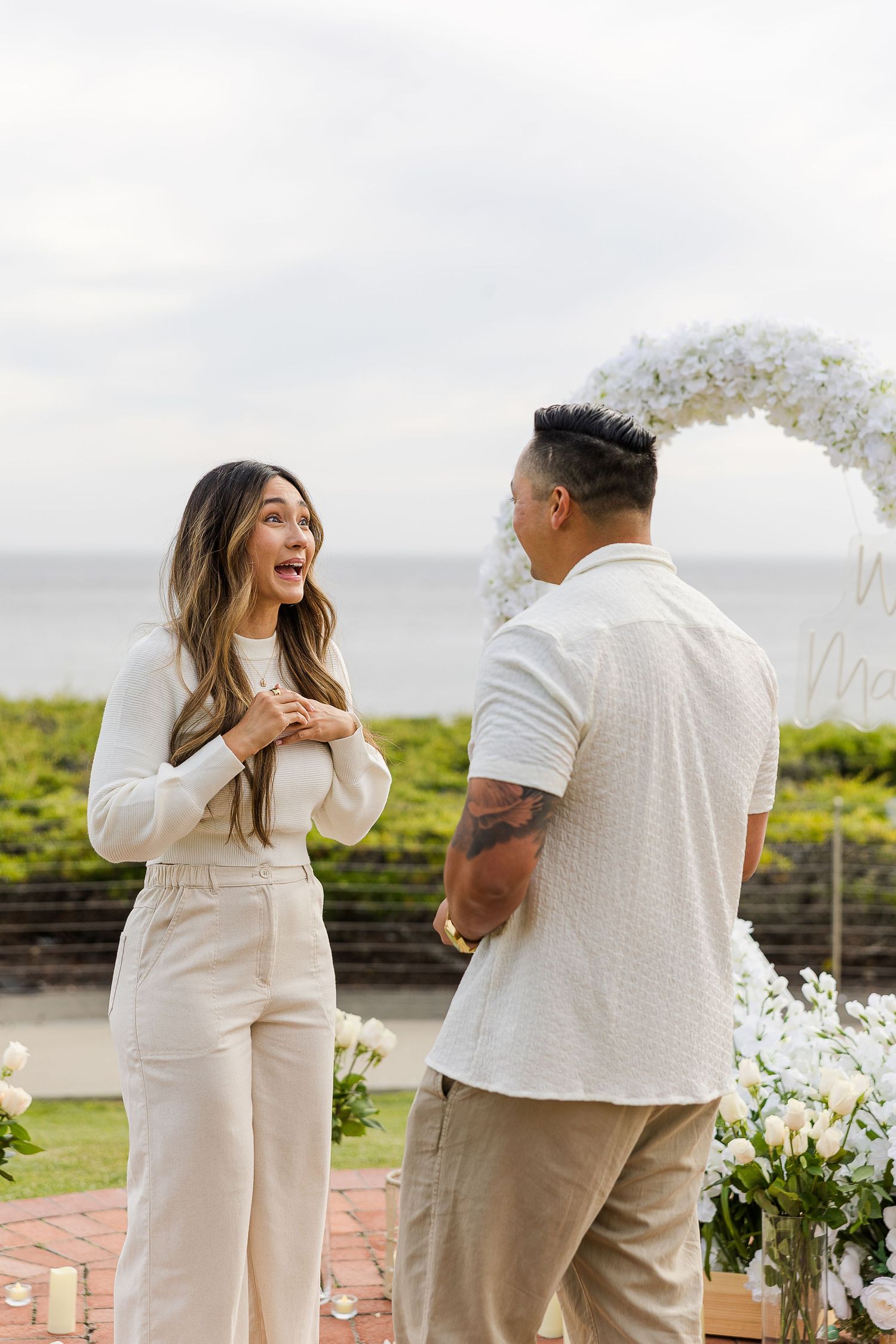 A joyful surprise proposal moment captured in a series of photos at an outdoor venue with white floral decorations.