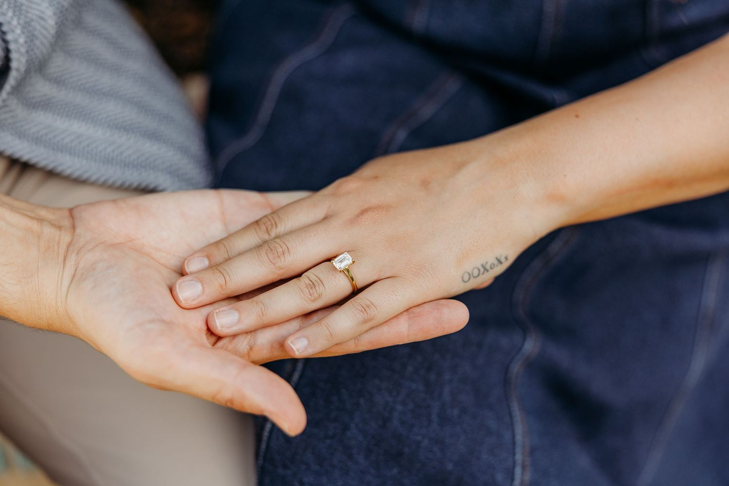 Close up of hands showing off an engagement ring against navy blue fabric.