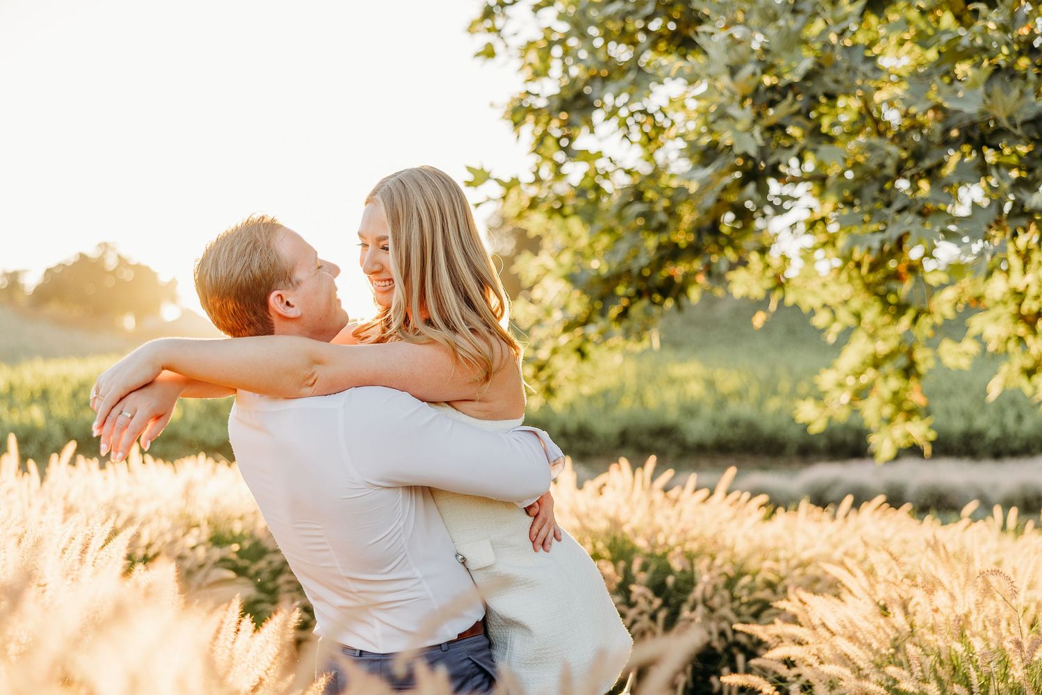 A couple embraces in a romantic moment surrounded by golden sunlight and trees in a garden setting.