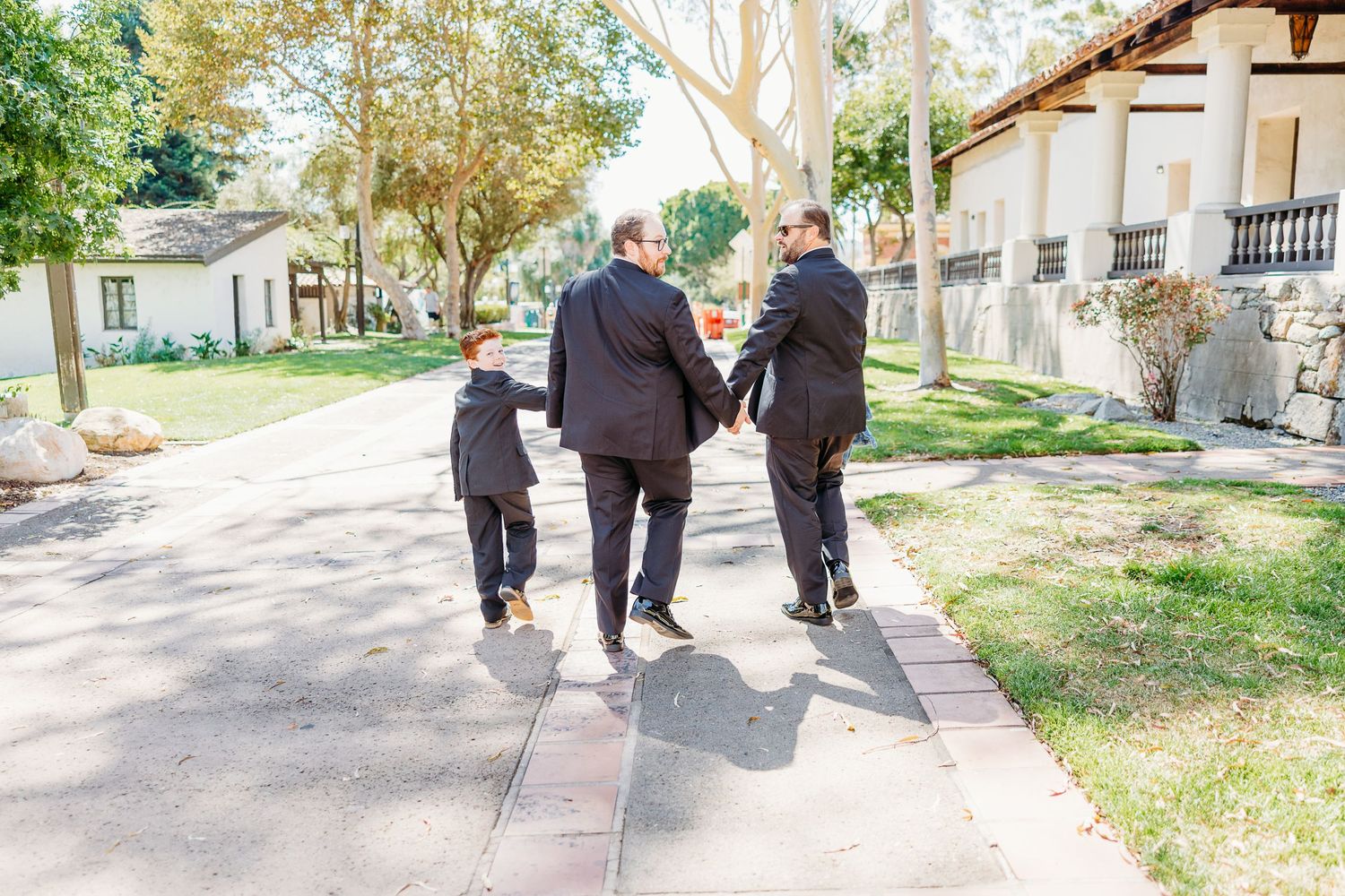 Three people walking together on sunny pathway through park grounds.