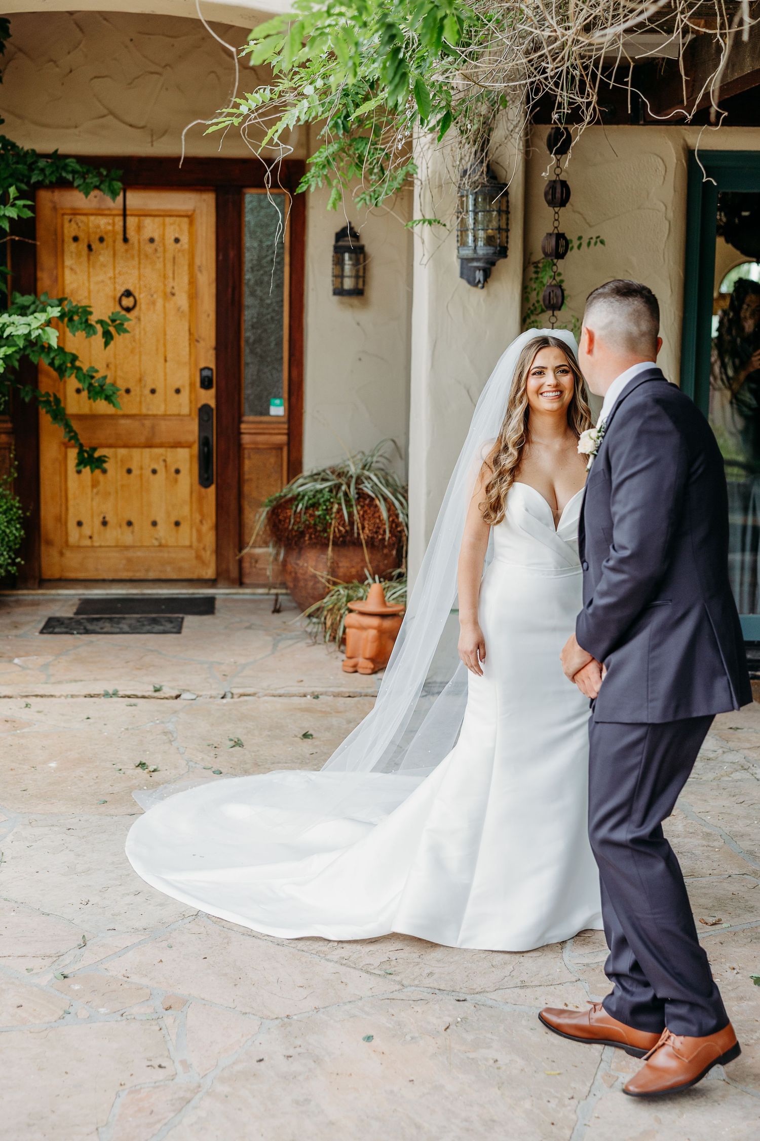 Wedding couple walking in a Spanish courtyard with rustic wooden doors and flowing white wedding dress train.