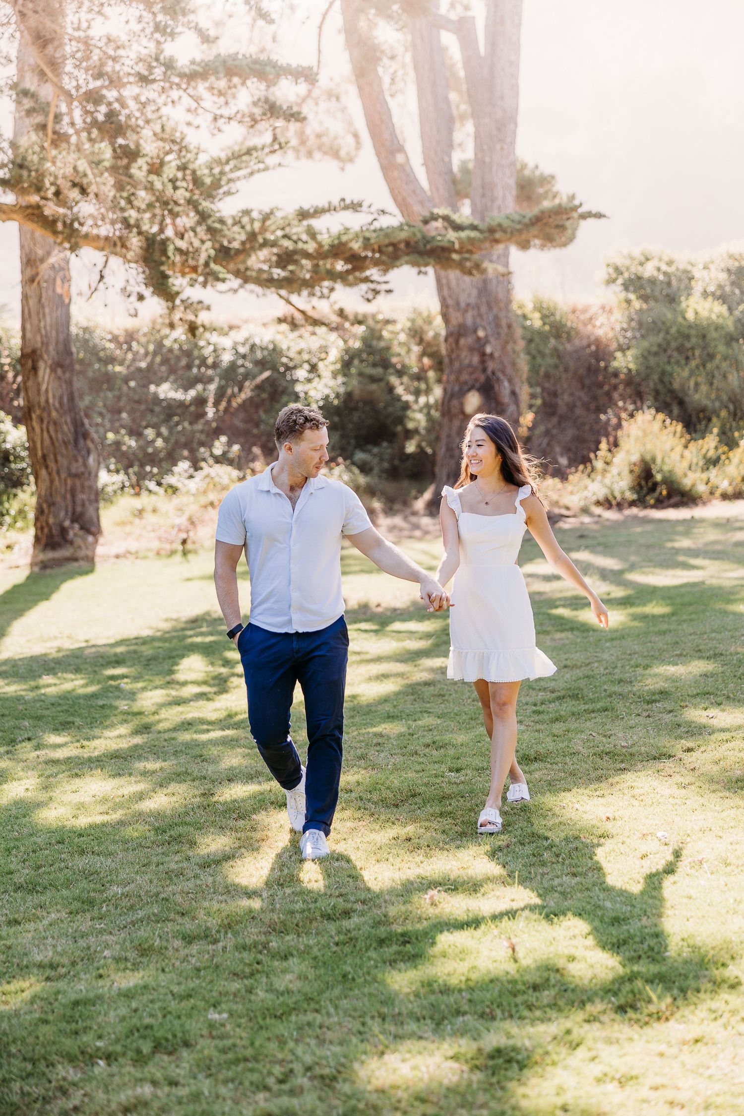 Joyful couple running together on grass path surrounded by trees.