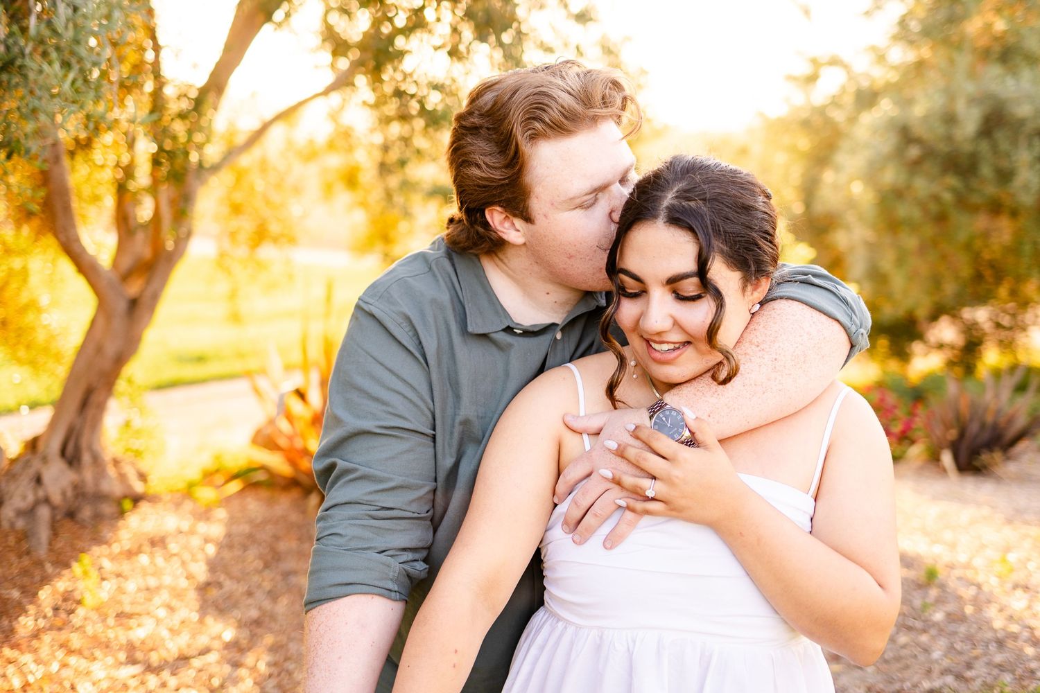 A romantic outdoor photoshoot in a natural setting with golden sunlight filtering through trees.