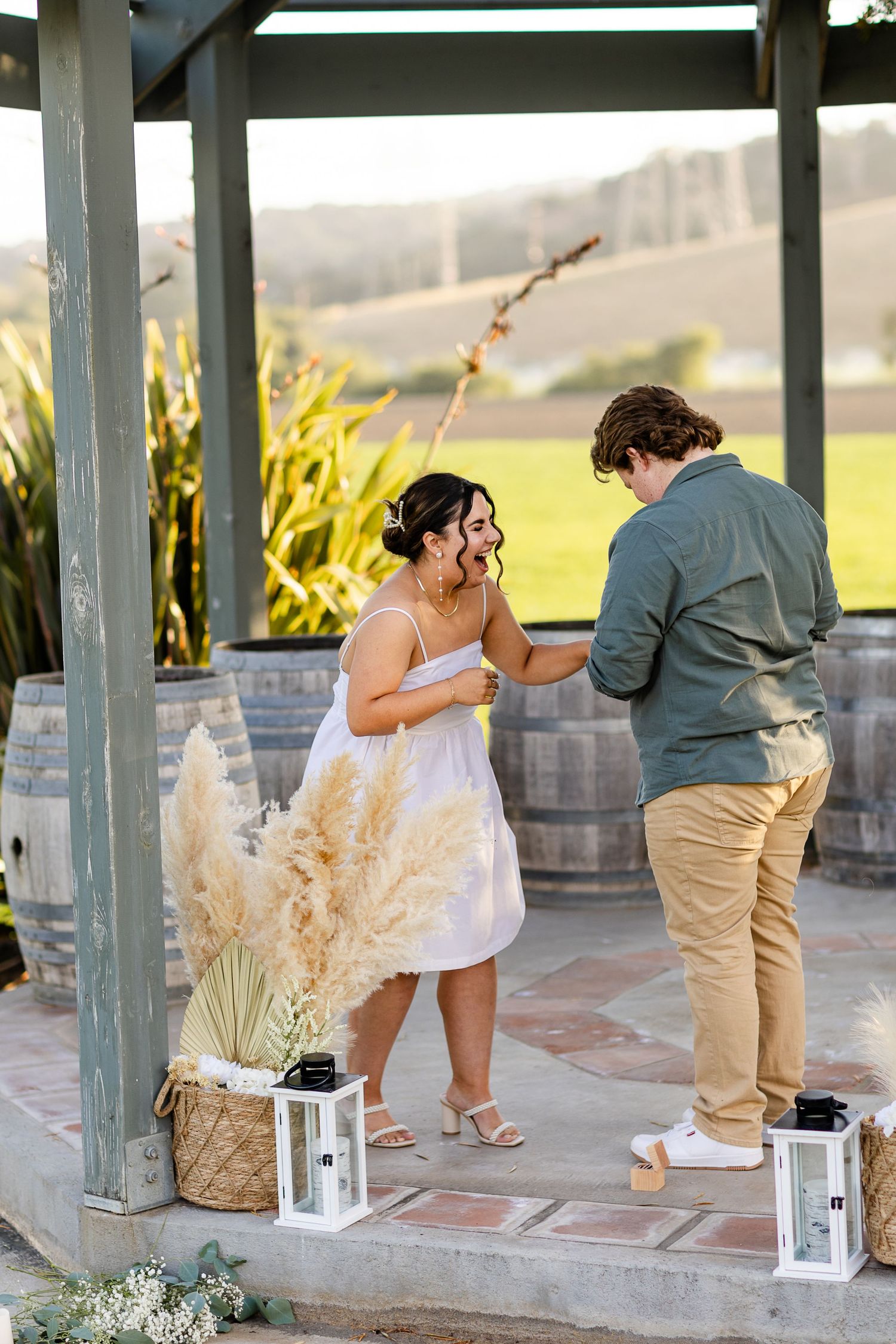 A romantic outdoor proposal moment takes place under a rustic gazebo with pampas grass and wine barrel decor.