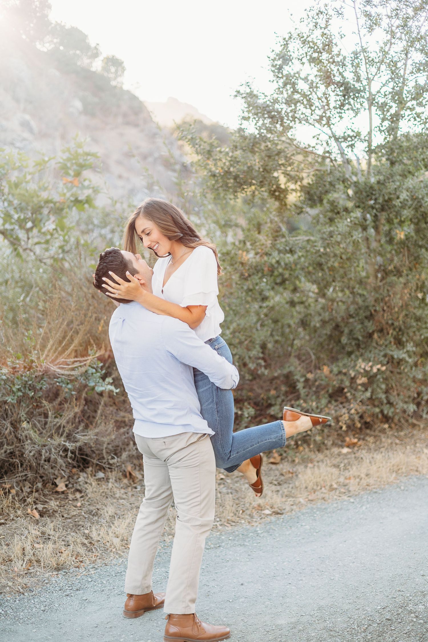 A playful embrace on a sunlit path with natural scenery in the background.