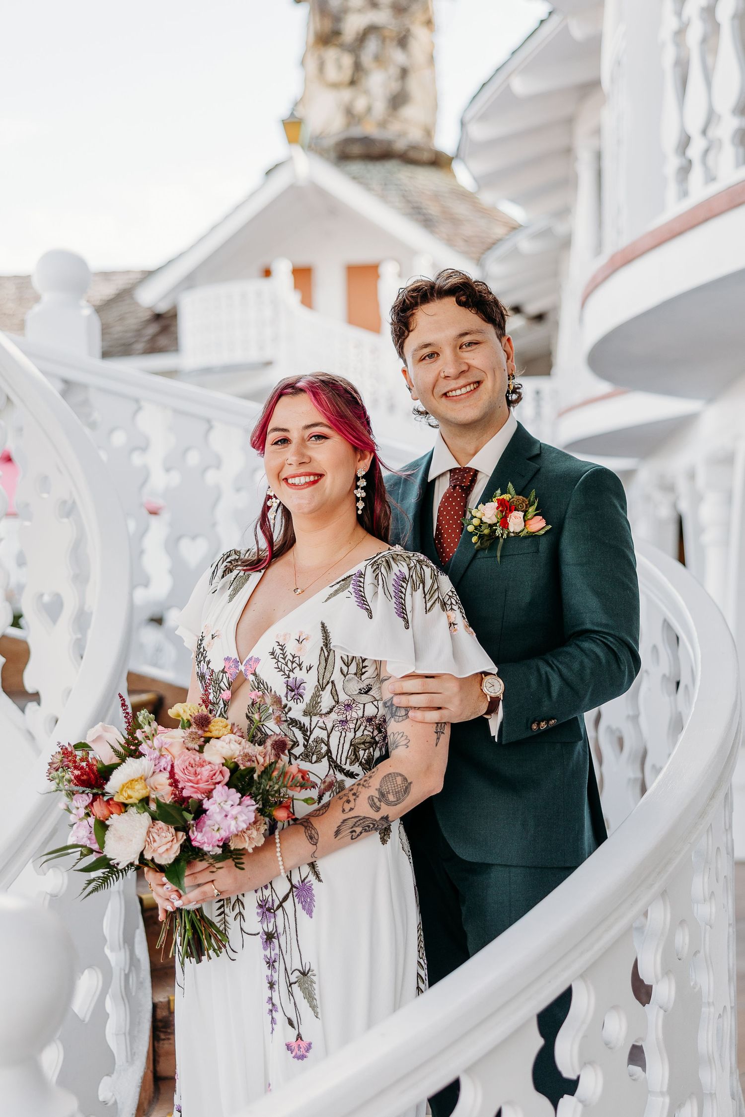 Wedding couple posing on white decorative stairs with floral bouquet.