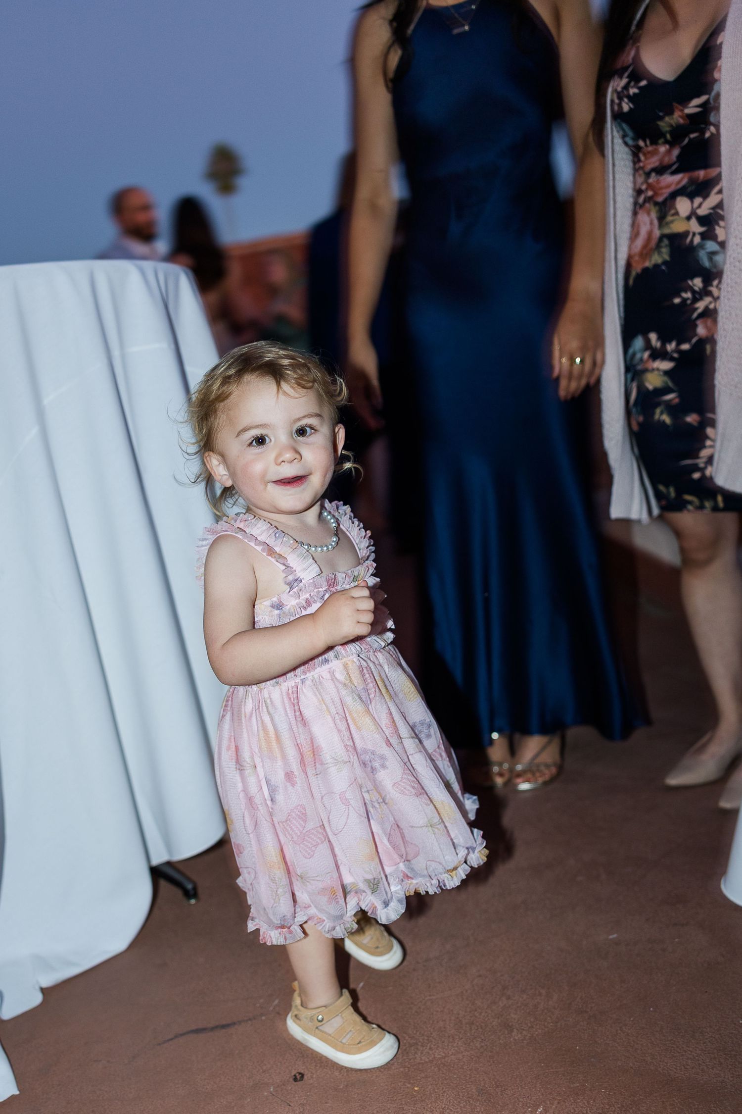 A small child in a pink dress toddles across the dance floor at a wedding reception.