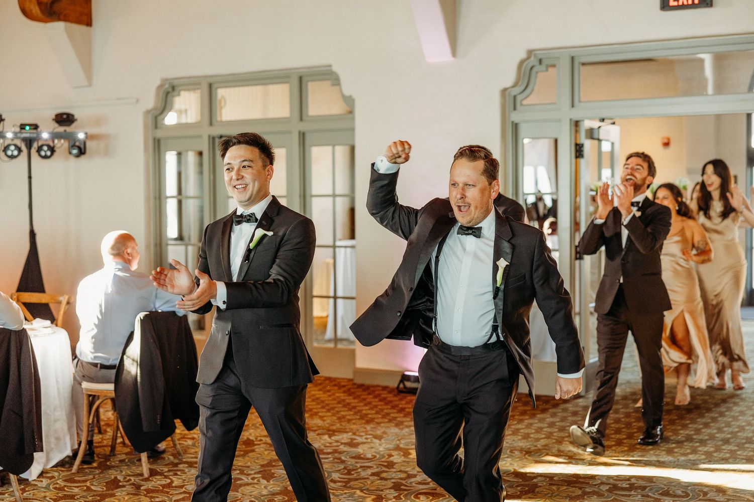 Wedding guests dancing and celebrating with joyful expressions in an elegant indoor venue.