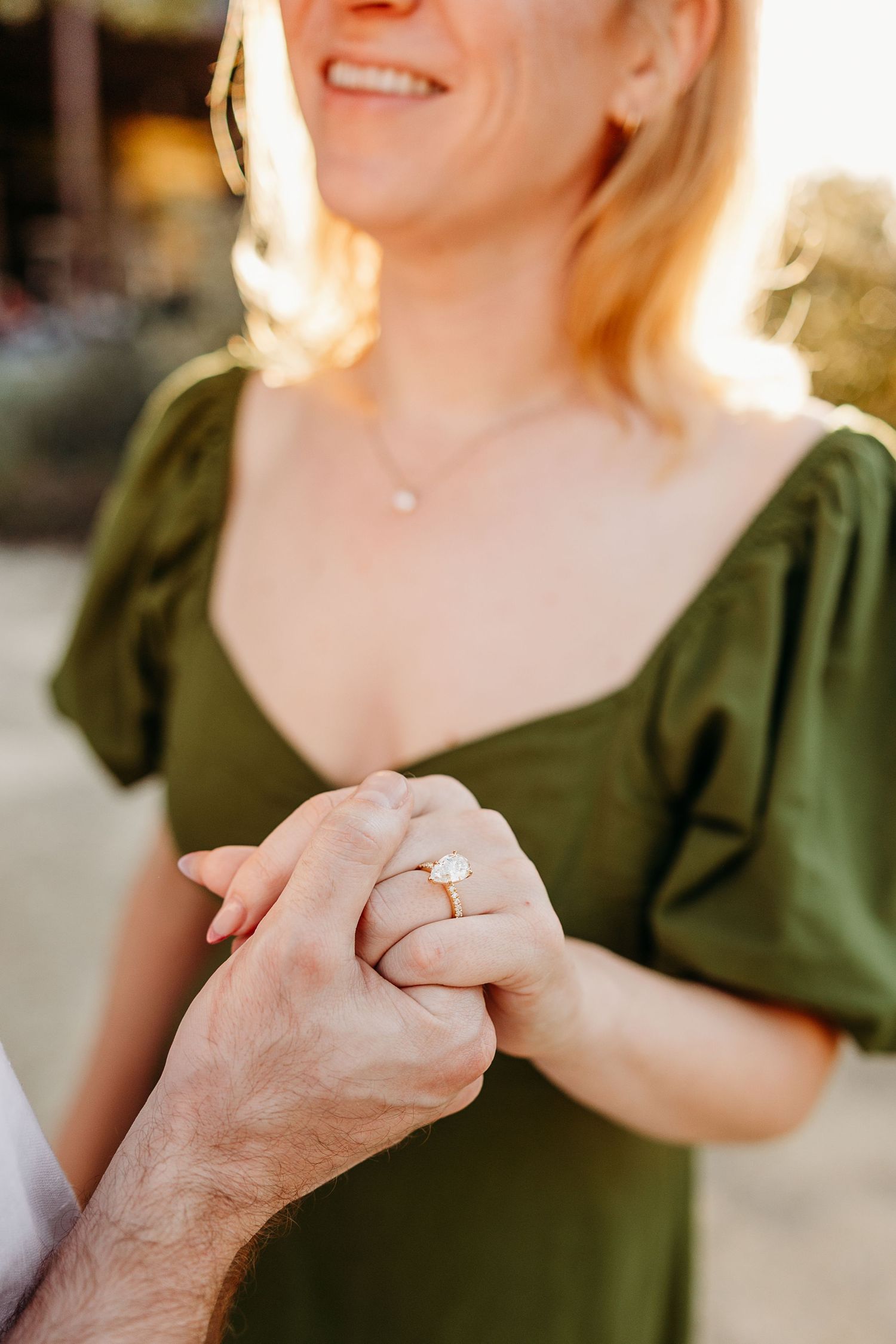Close-up shot of hands holding together with an engagement ring sparkling in the sunlight.
