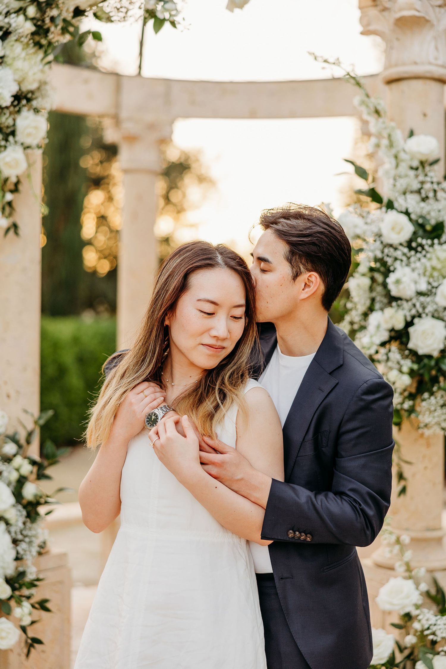 Intimate moment between couple under floral-decorated pergola during sunset.