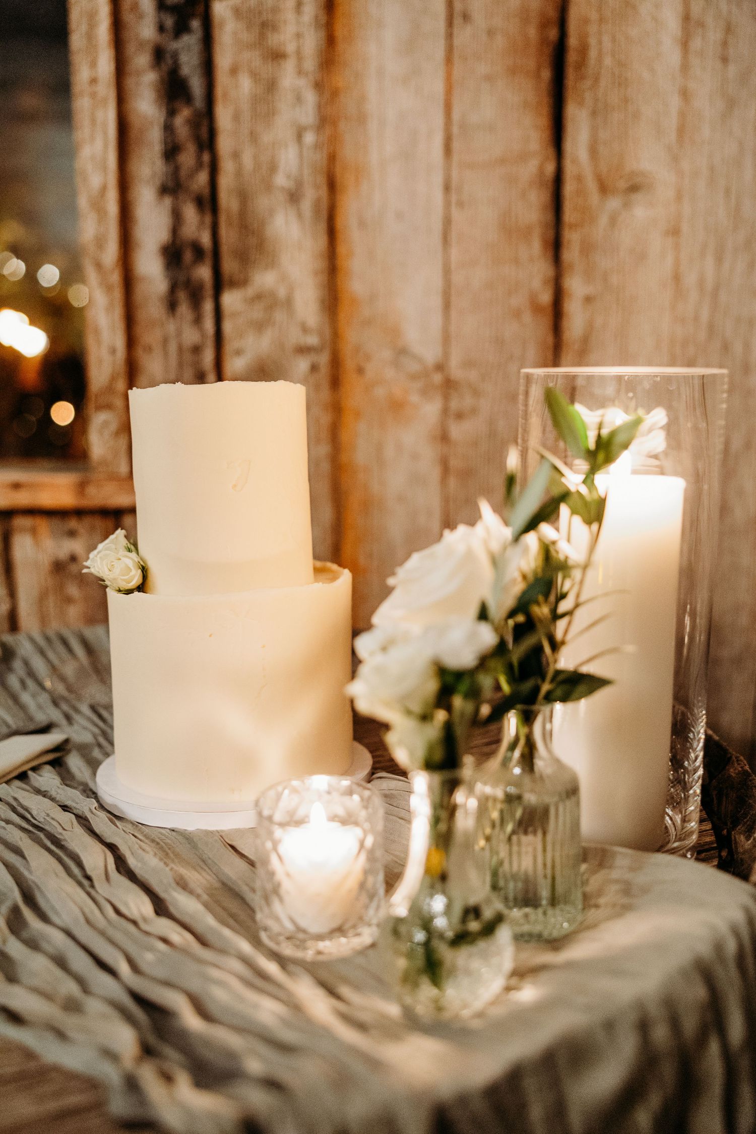 Rustic wedding decor featuring white candles and roses against weathered wooden backdrop.