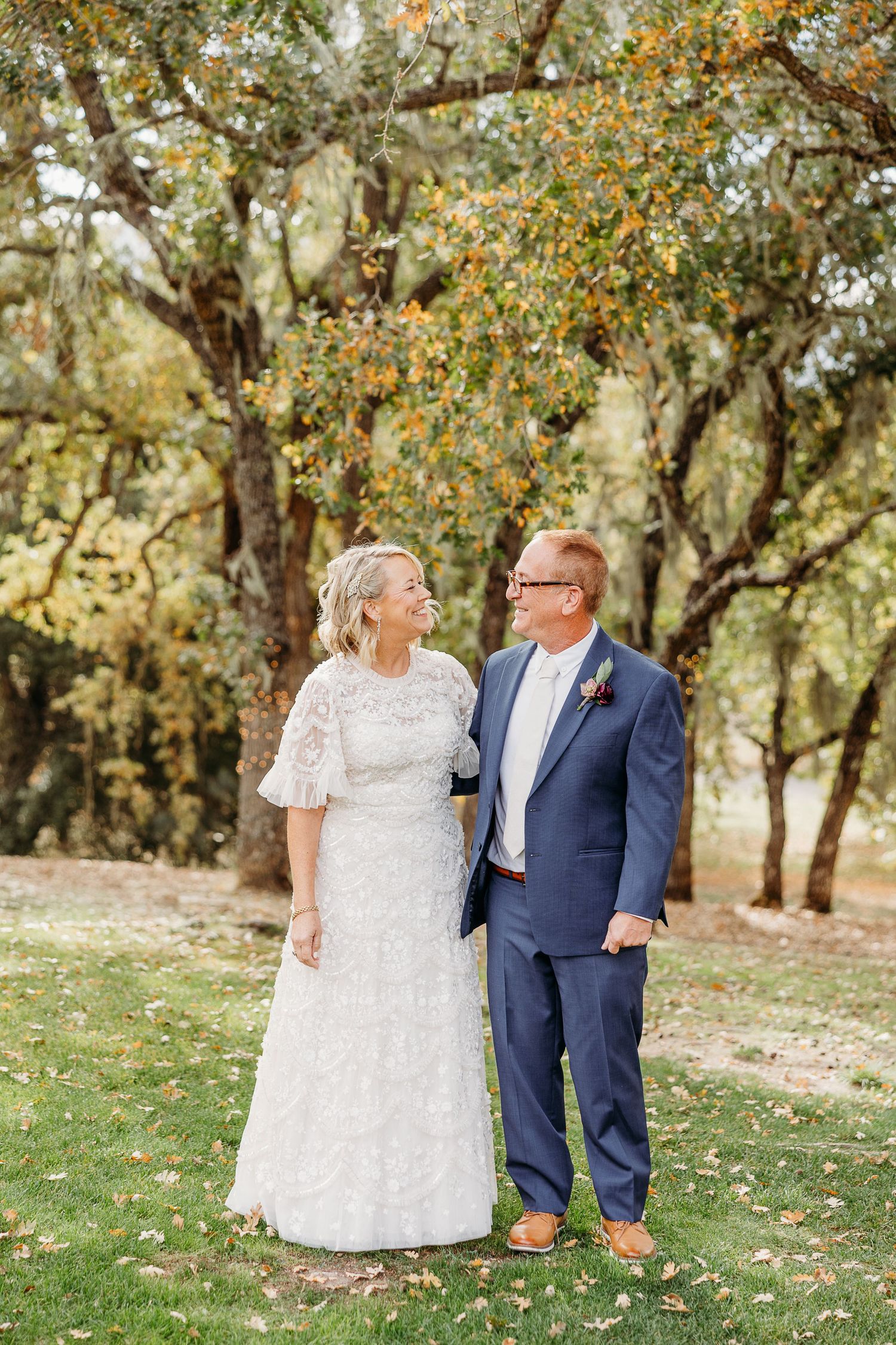 Newlyweds share intimate moments together during autumn wedding photoshoot under golden trees.