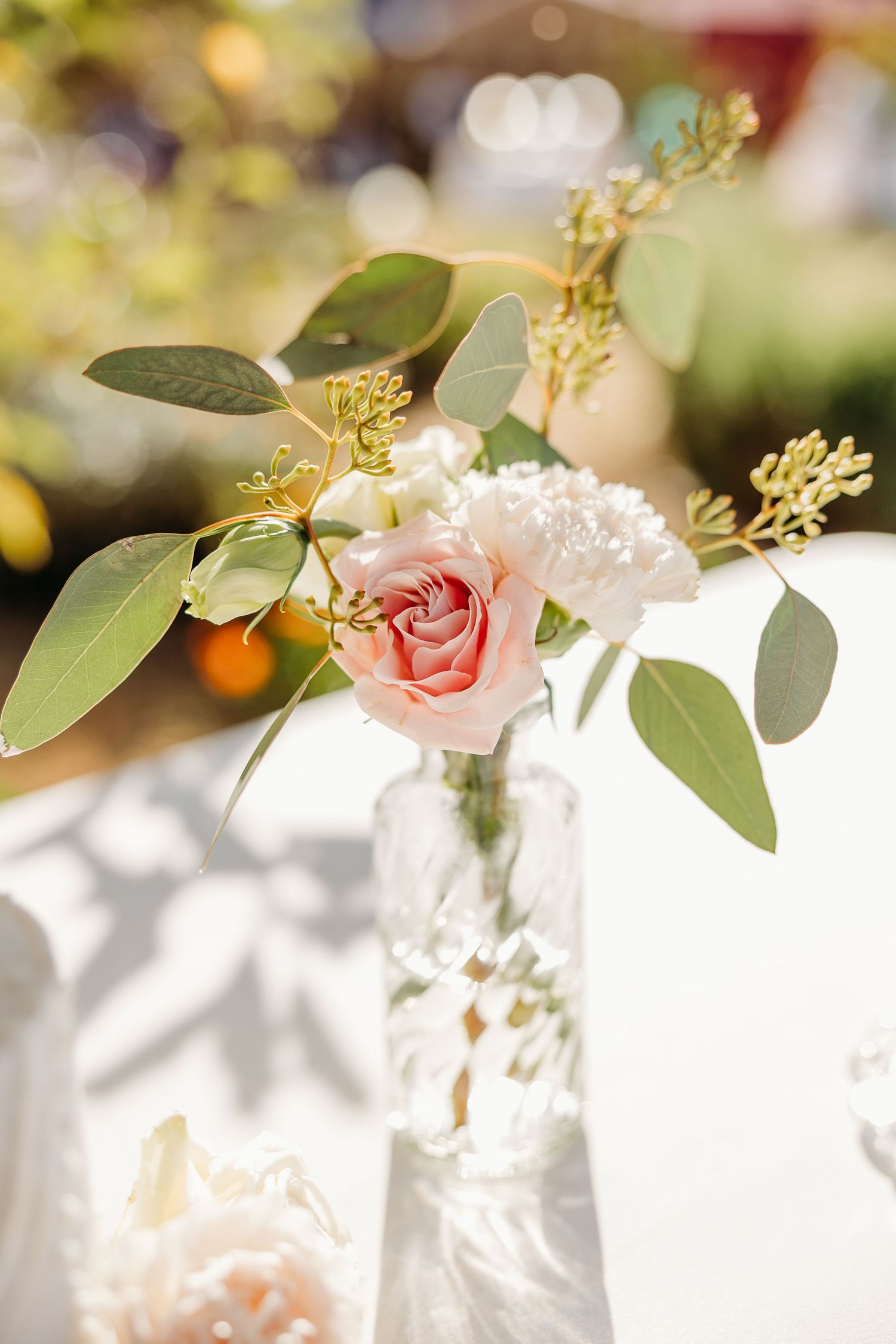 Delicate floral centerpiece with pink roses and eucalyptus leaves on white tablecloth.