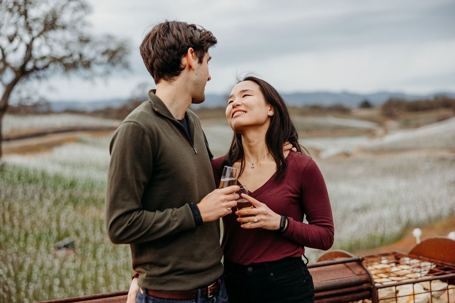 A couple shares a romantic moment while sitting together on a scenic hillside during sunset.