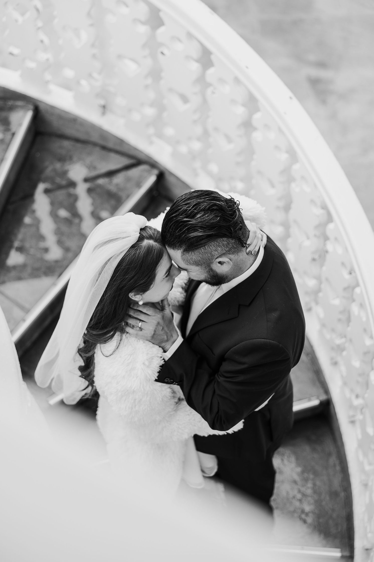 A black and white intimate wedding photo shows a tender romantic moment between newlyweds under an archway.
