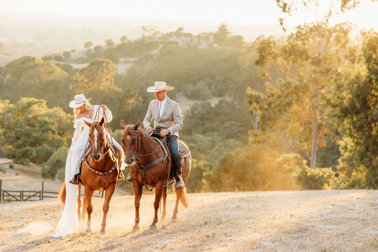 Two riders on horseback traverse a scenic mountain trail at sunset.