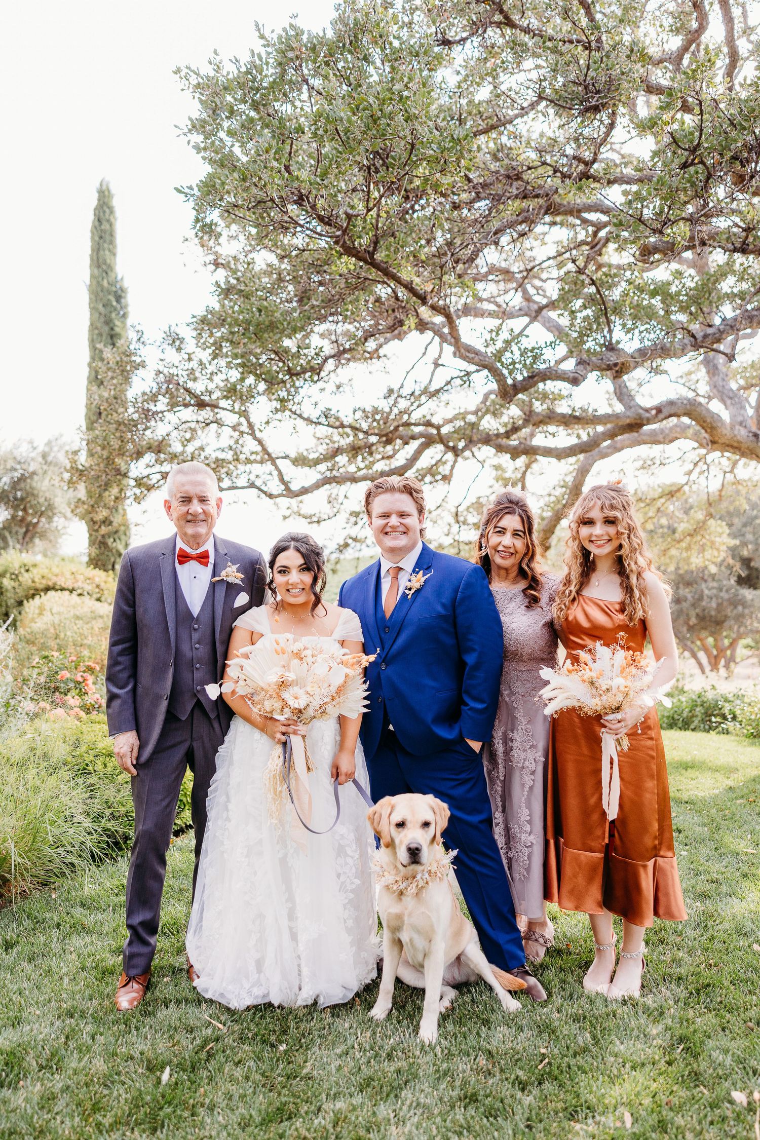 Family portrait with yellow lab at outdoor wedding featuring rust-colored bridesmaid dresses.