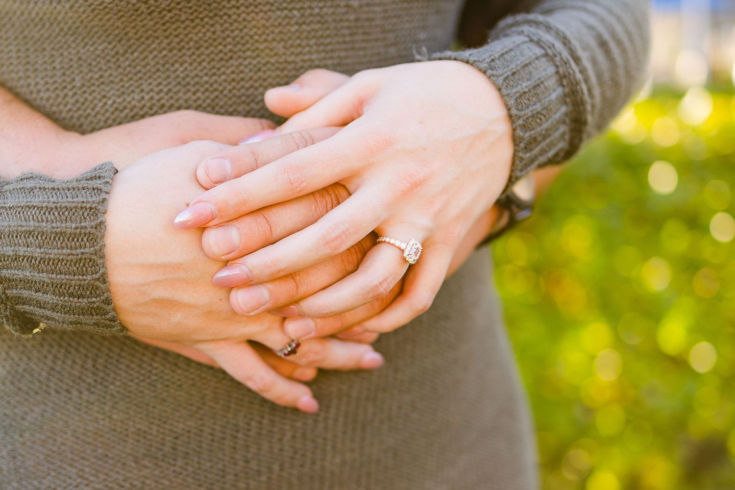 Intimate close-up of hands gently embracing, showcasing an engagement ring.