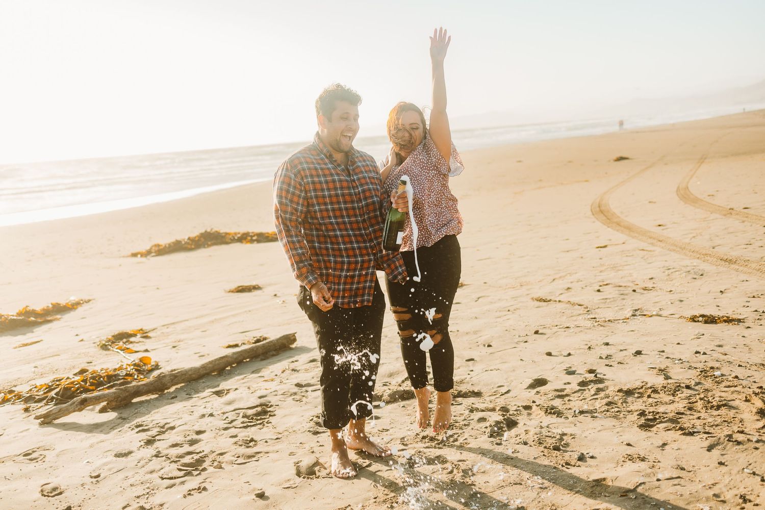 A couple celebrating on a sunny beach with their arms raised in joy during sunset.