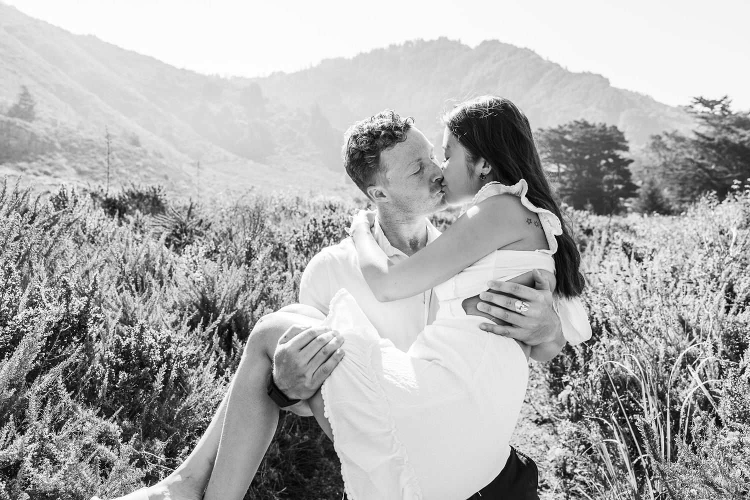 Black and white photo of a couple sharing an intimate moment in front of mountain scenery.