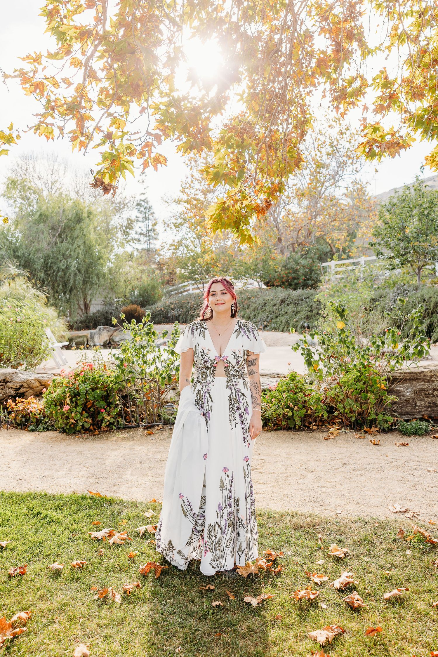 Autumn wedding portrait in a garden with golden sunlight and fallen leaves.