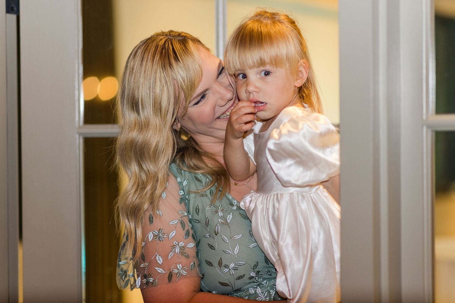 Sweet candid moment between parent and child in formal attire by a window.