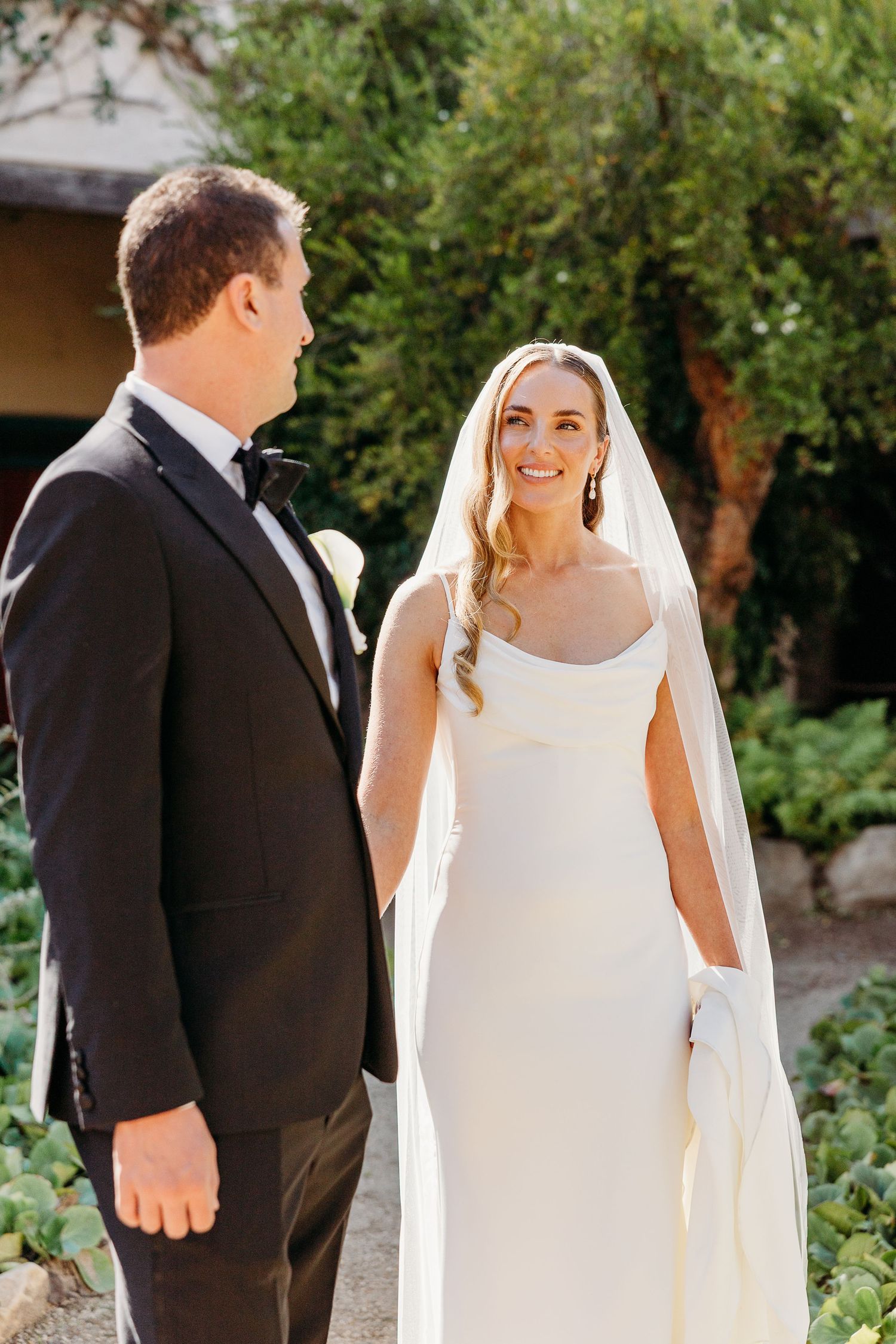 A bride and groom share a romantic first look moment in a lush garden setting.