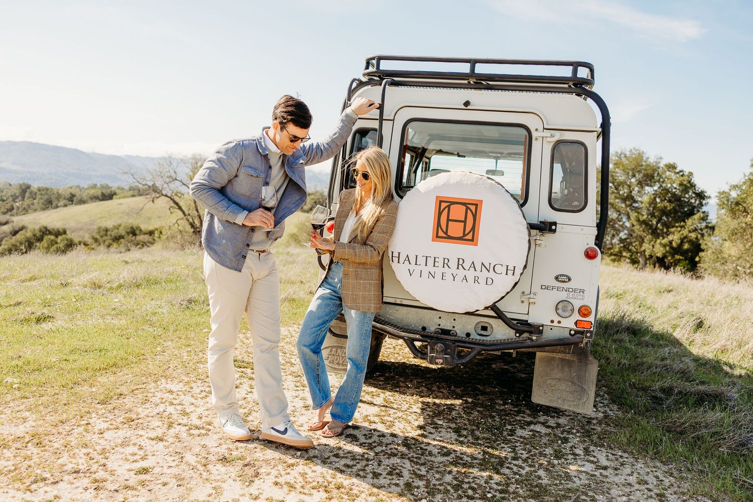 A couple unpacks camping gear from their trailer while enjoying an outdoor adventure in a scenic mountain setting.