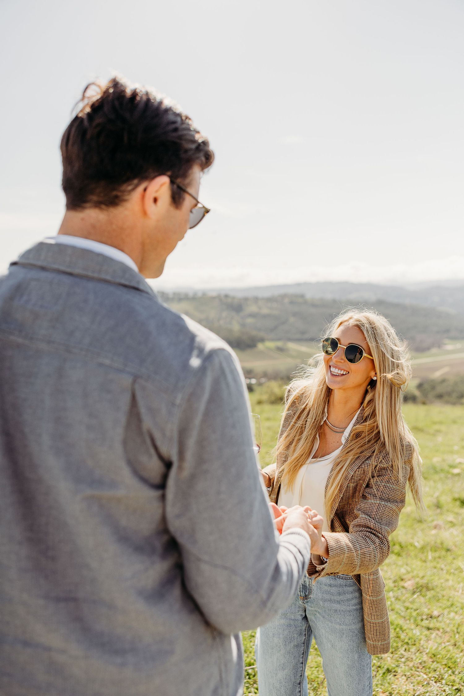 Joyful interaction between couple on sunny hillside with scenic mountain backdrop.
