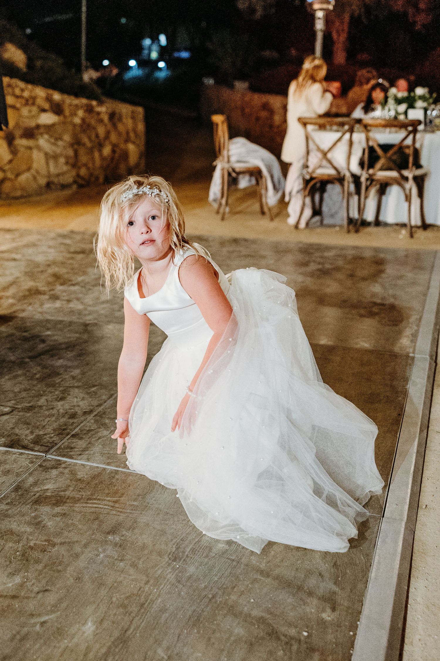 A young flower girl in a white tulle dress twirls on the dance floor at a wedding reception.