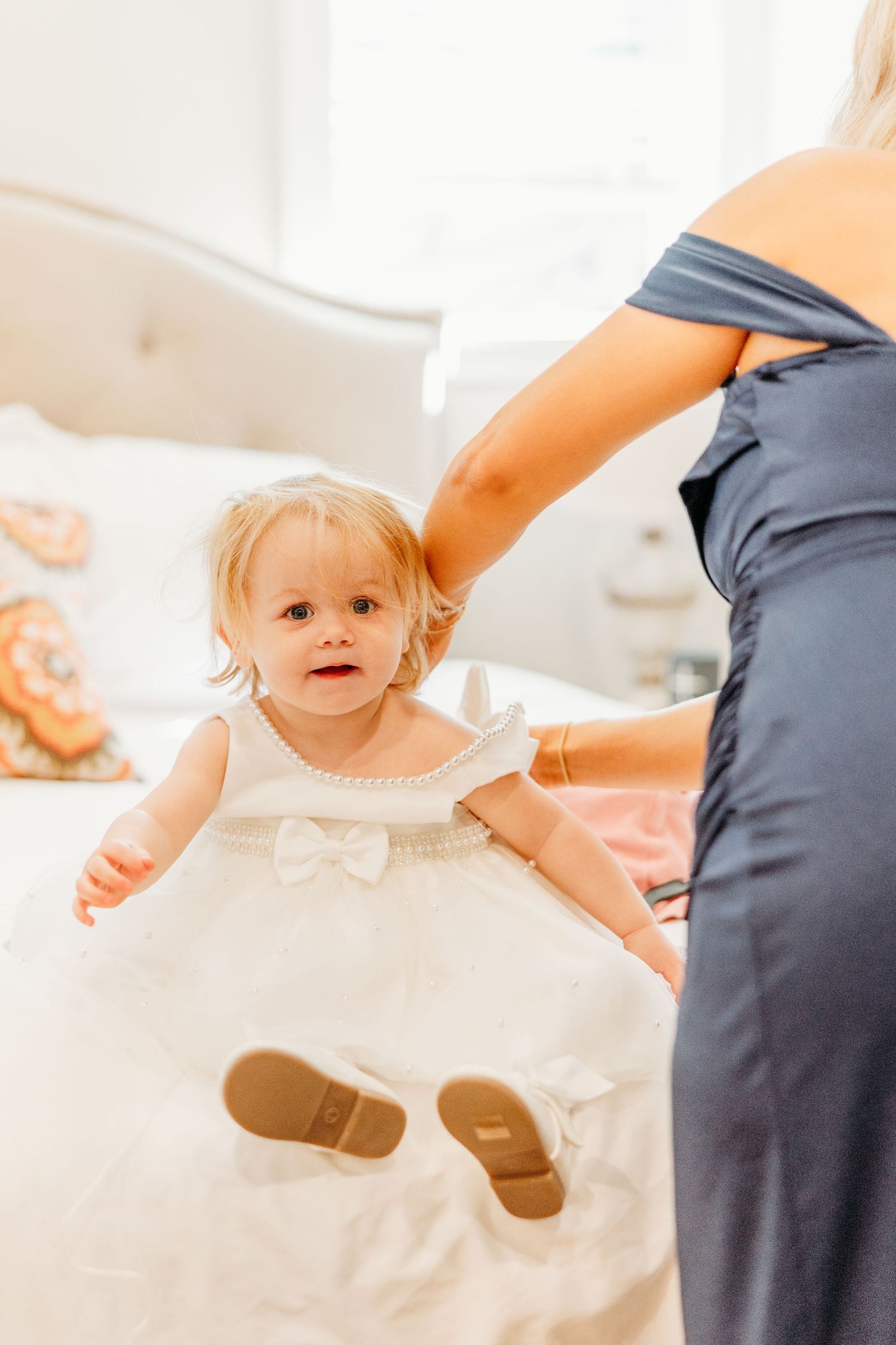 A small child in a white dress reaching up during a special occasion.
