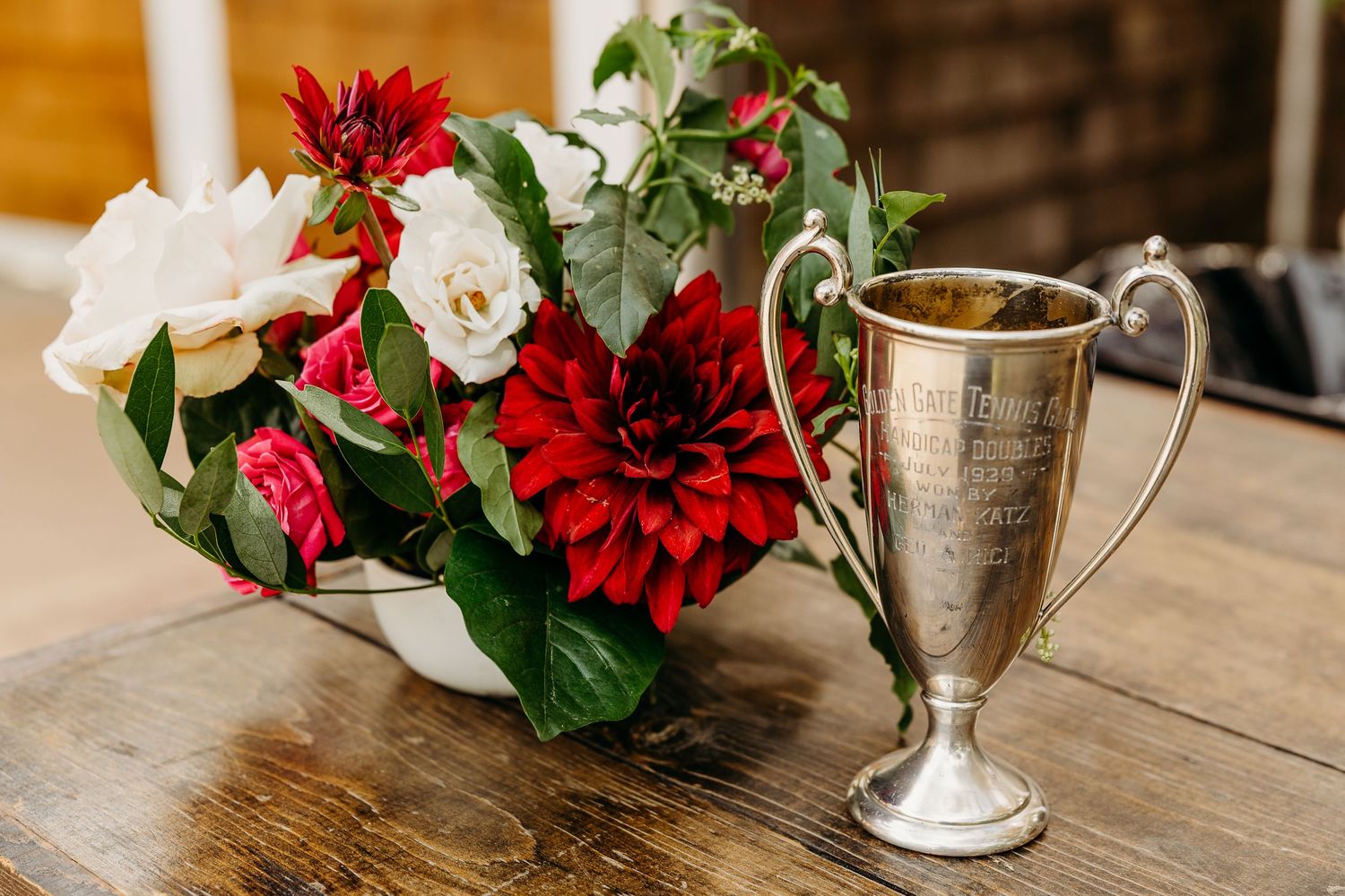 Red and white floral arrangements with silver vases on rustic wooden tables.