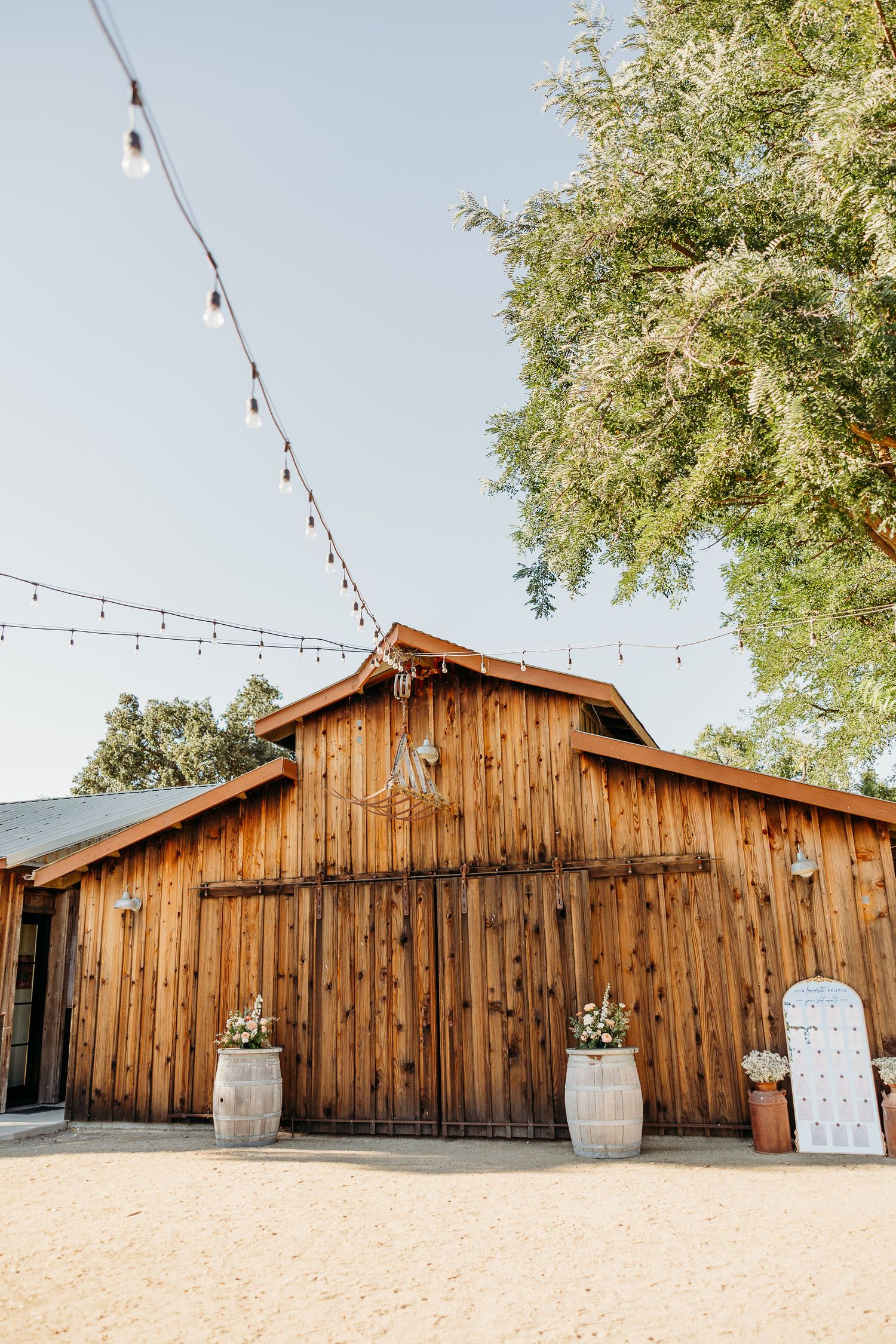 Rustic wooden barn venue with string lights and wine barrels creates a charming outdoor wedding setting.