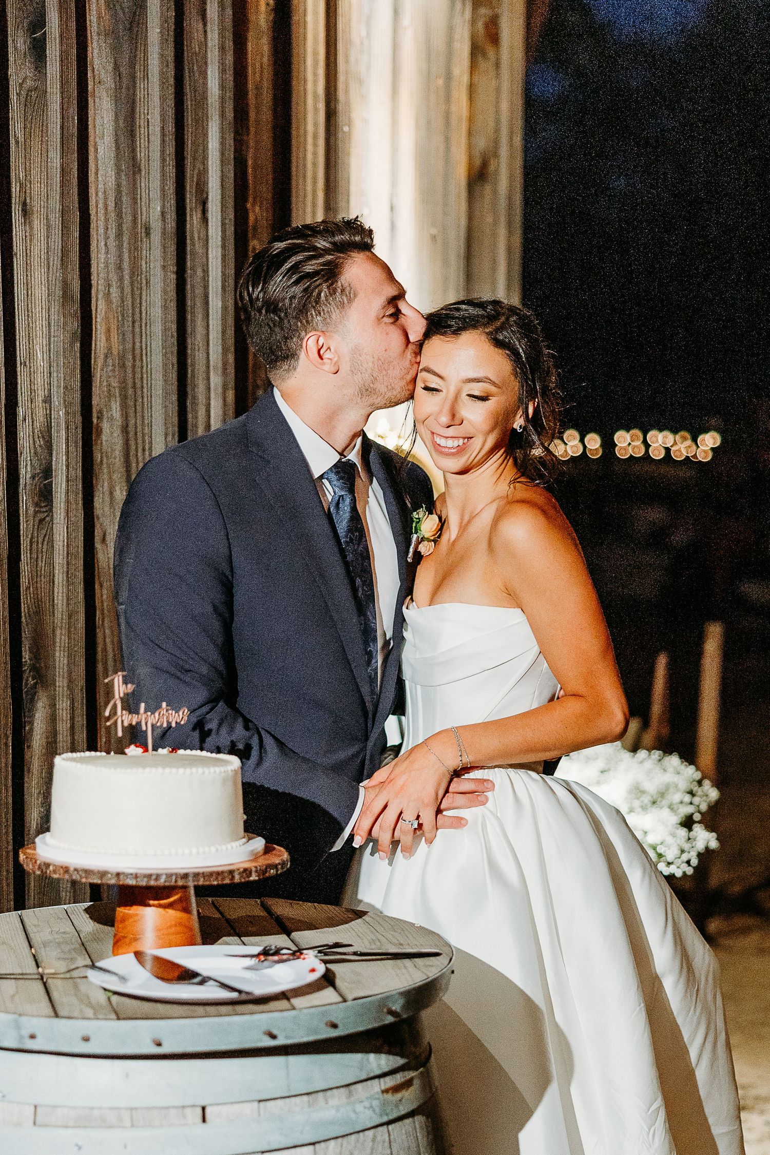 Newlyweds share an intimate moment while cutting their wedding cake in a rustic venue.