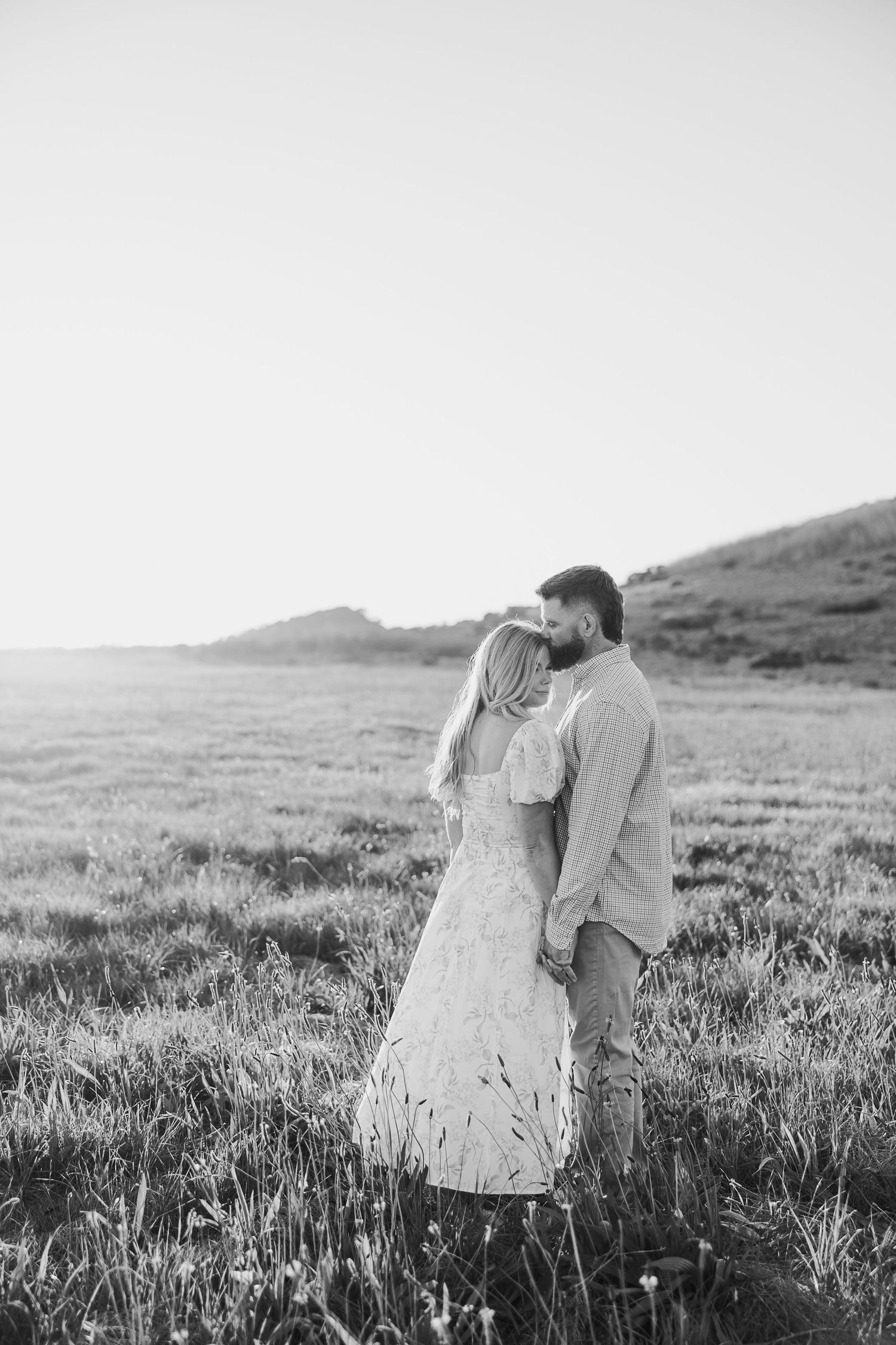 A couple shares an intimate black and white moment in a rolling grass field.
