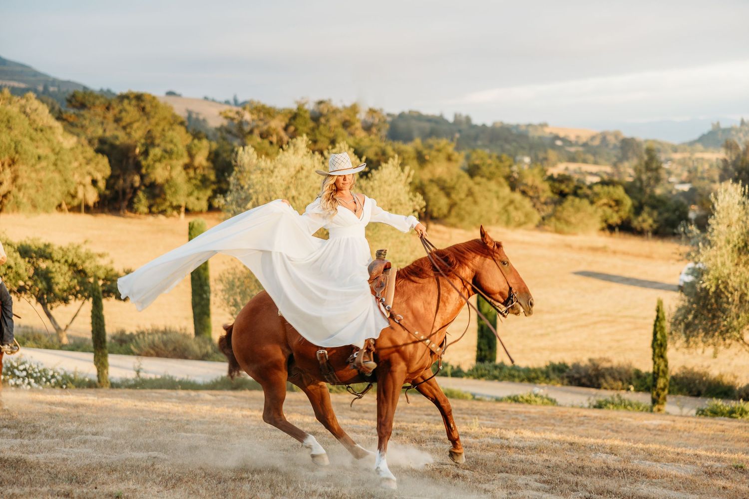 A flowing white dress billows dramatically while horseback riding on a scenic mountain trail.