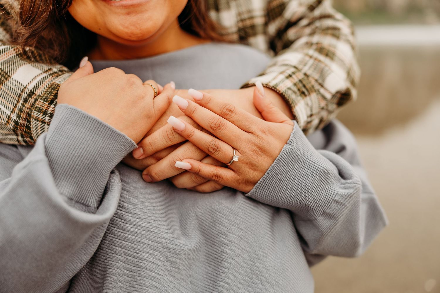 A close-up of hands embracing on a gray sweater against a blurred background.