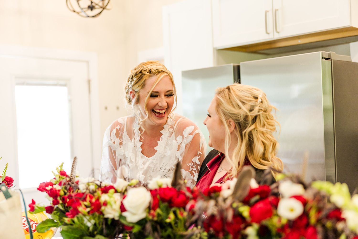 Two people share a joyful moment while getting ready with red and white floral arrangements.