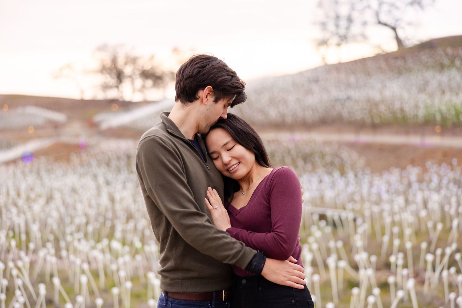 A romantic couple embracing in a field of flowers during sunset.