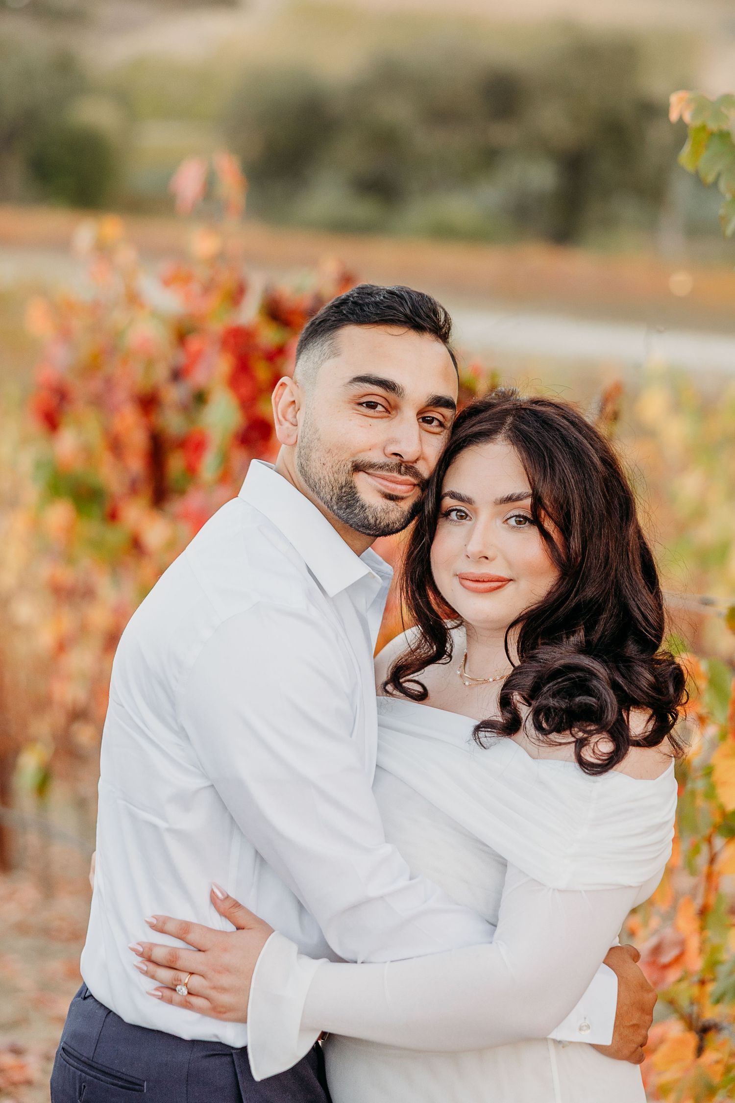 A couple embraces in a romantic photoshoot among autumn vineyard vines with golden foliage at sunset.